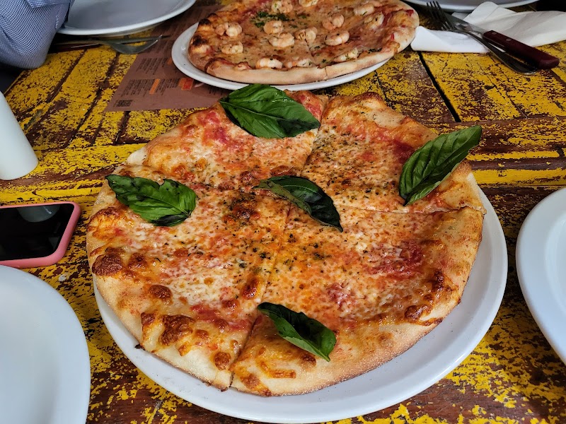 Pizza de masa fina con queso dorado y hojas de albahaca en Tiramisú